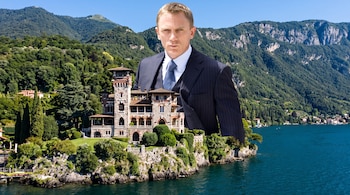 Primer plano de Daniel Craig en traje, superpuesto sobre la fachada de una villa de piedra junto a un lago rodeado de montañas y vegetación.