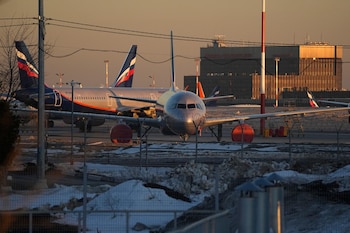 Avión Aeroflot plateado en pista de aeropuerto con nieve. Otros aviones y la terminal Sheremetyevo de Moscú al fondo, vistos a través de una valla
