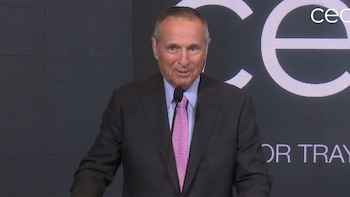 Hombre con traje oscuro y corbata rosa frente a un micrófono. Detrás, una pantalla con el logotipo "ceo" y parte de la frase "FOR TRAV"