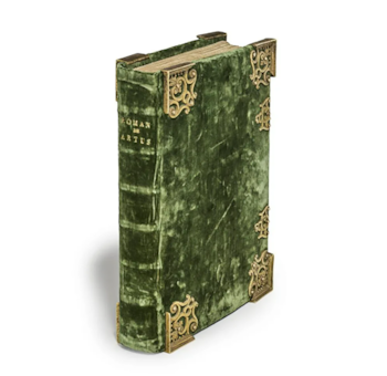 Primer plano de un libro antiguo de tapa dura, con encuadernación de terciopelo verde y ornamentos dorados en las esquinas, mostrando la espina con el título 'ROMAN DE ARTUS'