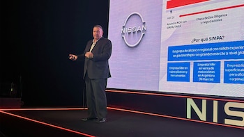 Un hombre con traje sobre un escenario junto a una pantalla con el logotipo de Nissan y un gráfico de presentación