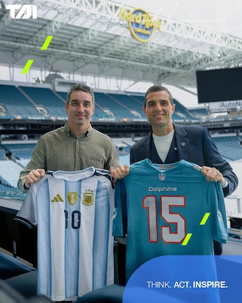 Dos hombres sostienen en un estadio una camiseta de la Selección Argentina y una camiseta turquesa de los Miami Dolphins