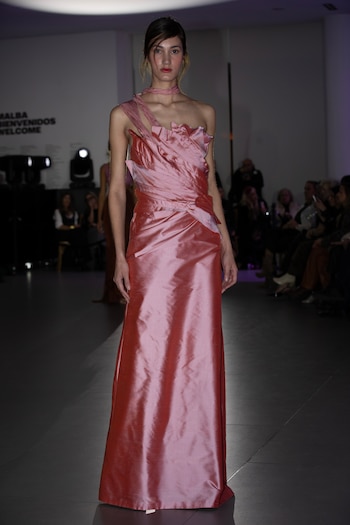 Modelo en la pasarela con un vestido largo de color rosa satinado con pliegues en el torso y escote asimétrico
