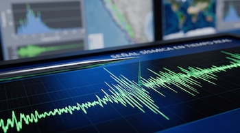 Una aguja metálica dibuja una gráfica de ondas en color verde brillante sobre una pantalla azul con mapas de fondo.