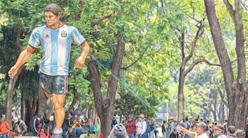 Dibujo a lápiz de color de una gran figura de un futbolista argentino con camiseta Albiceleste, en un parque con árboles y multitudes de personas.