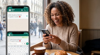 Mujer sonriendo escribe en un smartphone. Se ve un chat de WhatsApp para "Mamá" con un corazón. En la mesa, una taza de café y un croissant.