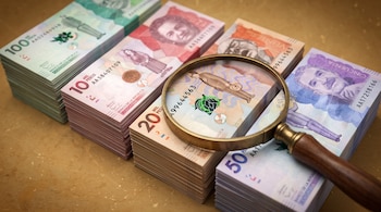 Cuatro fajos de billetes de pesos colombianos dispuestos en fila con una lupa metálica sobre uno de ellos.