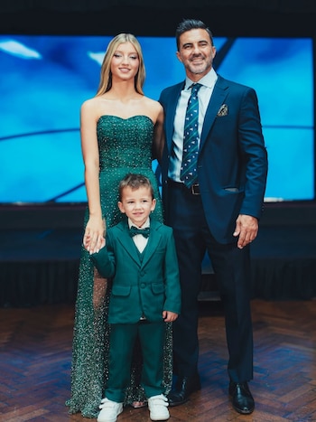 Fabián Cubero, sonriendo, de traje azul, junto a su hija Allegra, de vestido verde brillante, y su hijo Luca, de traje verde y pajarita