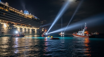 Varios botes de rescate con luces de búsqueda convergen en un gran crucero iluminado, operando en aguas tranquilas bajo un cielo nocturno en Bahamas.