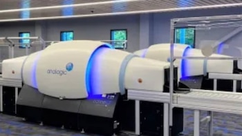 Dos máquinas de escaneo de equipaje de color blanco y negro con iluminación azul de la marca Analogic sobre cintas transportadoras