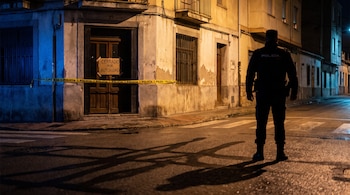 Un policía de espaldas observa un edificio con cinta de precinto policial y un cartel en la puerta que dice CERRADO POR AUTORIDAD.