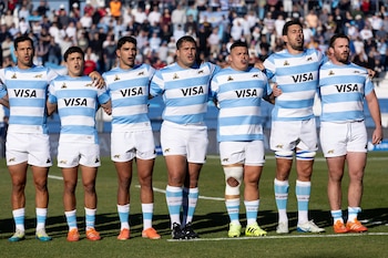 Siete jugadores de rugby con camisetas celestes y blancas a rayas, shorts blancos y medias celestes y blancas están de pie en una cancha de césped