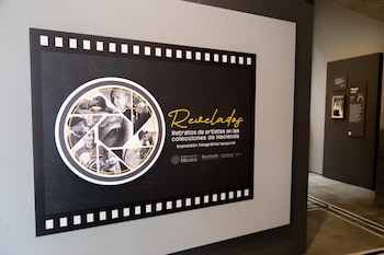 Panel informativo con el título Revelados y un diseño de obturador con retratos en blanco y negro dentro de una galería de arte