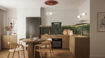 Cocina con gabinetes superiores blancos, gabinetes inferiores de madera, azulejos verdes, refrigerador, horno, estufa, fregadero, mesa redonda con cuatro sillas, y lámparas.