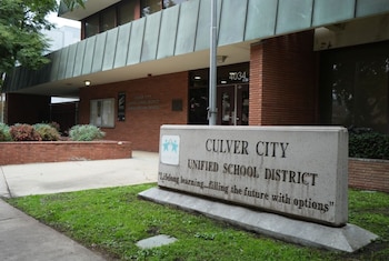 Un letrero de concreto con el texto Culver City Unified School District frente a un edificio de ladrillo rojo con vegetación