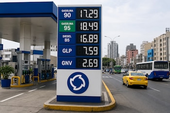 Cartel digital con precios de combustibles, surtidores de estación de servicio y vehículos en una avenida urbana.