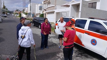 Varias personas, algunas con chalecos y cascos de seguridad, alrededor de un vehículo de emergencia con logotipo de CONRED en una calle residencial junto a un perro