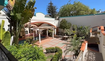 Patio interior con piscina, una estructura con columnas blancas, plantas, palmeras y muros de color blanco y terracota