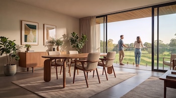 Un comedor con mesa de madera, sillas y aparador, junto a un balcón donde un hombre y una mujer observan un parque arbolado