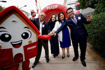 Mascota de Inabif en forma de casa roja y blanca junto a cuatro personas sonrientes, dos hombres y dos mujeres, frente a un arco inflable rojo con el logo INABIF