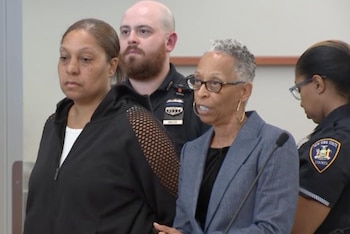 Mujer de chaqueta negra, dos personas con uniforme policial, y una mujer con cabello gris y gafas que habla en un micrófono en un entorno judicial