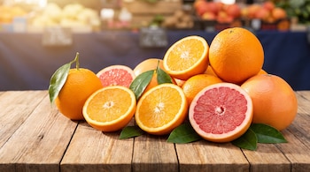 Naranjas y pomelos enteros y cortados a la mitad con hojas verdes sobre una mesa de madera.