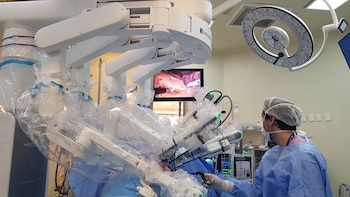 Un cirujano con vestimenta azul y mascarilla opera un robot médico cubierto con plásticos en un quirófano