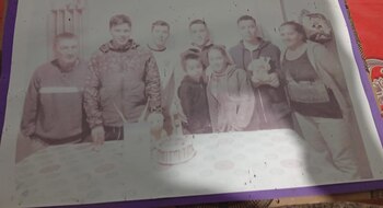 Fotografía sepia o muy descolorida que muestra a ocho personas, siete adultos y un niño, posando alrededor de una mesa con un pastel de cumpleaños. La imagen está deteriorada