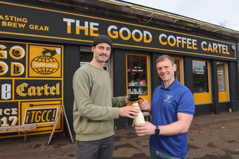 Bryce Cunningham dando una botella de leche al barista Jacob Smith frente a The Good Coffee Cartel en Glasgow, Escocia (Mossgiel Organic Dairy vía AP)