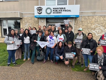 Un grupo de personas sostiene carteles y un pañuelo blanco frente al edificio del Ministerio Público Fiscal de Río Negro en Bariloche