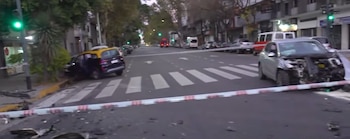 Un automóvil plateado gravemente dañado y un SUV negro (taxi) chocados en una intersección urbana, con escombros esparcidos y cinta policial visible
