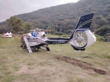 Helicóptero con la cabina destruida y las palas del rotor caídas sobre la hierba junto al agua
