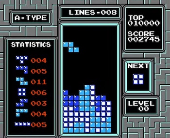 Pantalla de videojuego Tetris. Se ven el campo de juego con bloques azules, paneles de estadísticas, líneas, puntuación, siguiente pieza y nivel de juego