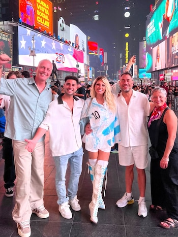 Cinco personas de pie en una plaza urbana nocturna con pantallas publicitarias luminosas de fondo. Una mujer lleva una camisa con el número 10