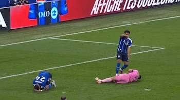 Tres futbolistas en un campo de césped. Uno de pie, otro arrodillado con camiseta azul y número 24, y el tercero tendido con camiseta rosa.
