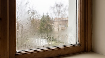 Ventana con marco de madera cuyo cristal presenta condensación y gotas de agua acumuladas en sus esquinas.