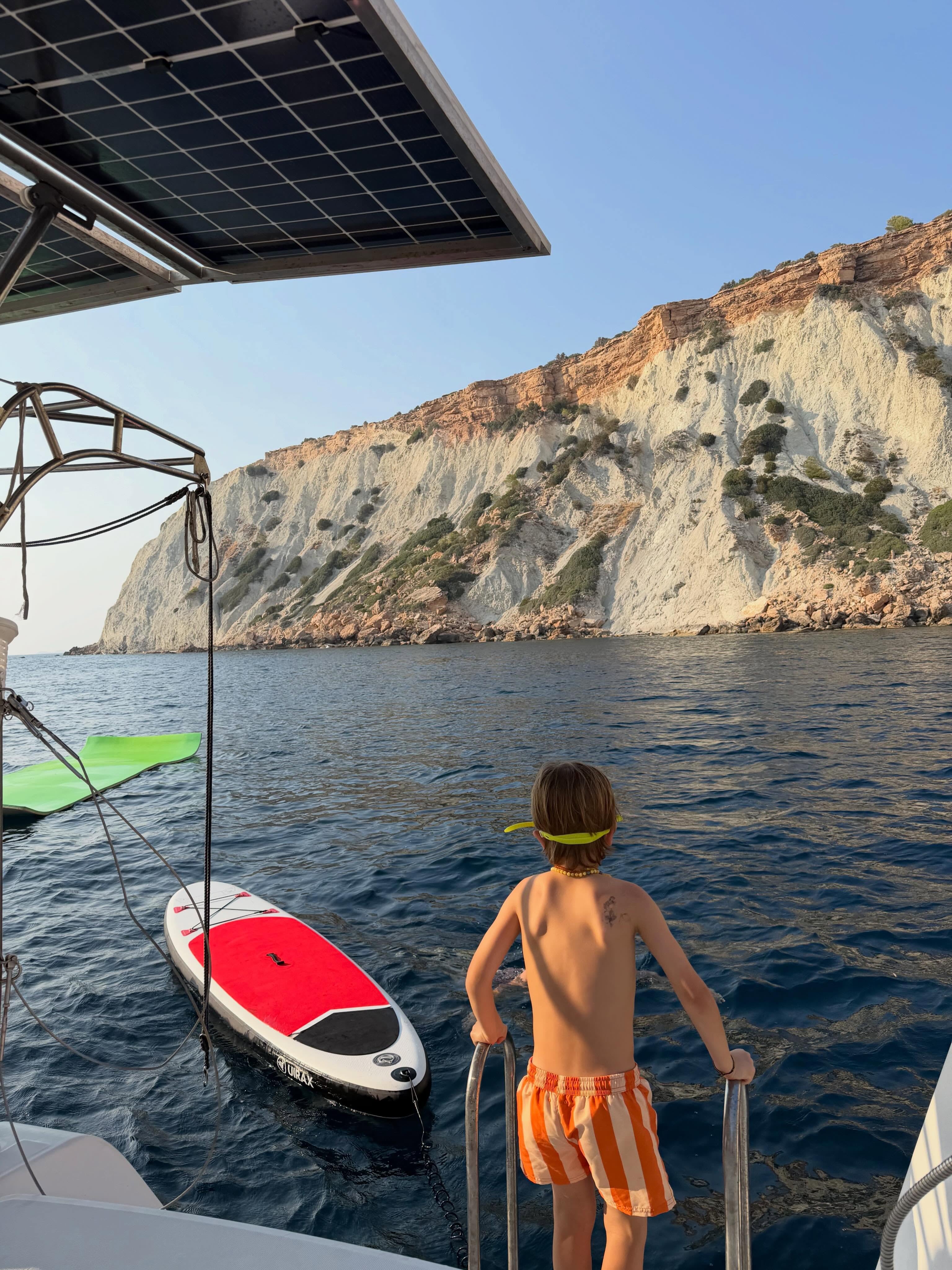 Viggo observa el mar y los acantilados de Ibiza desde la popa de una embarcación con elementos recreativos a flote.