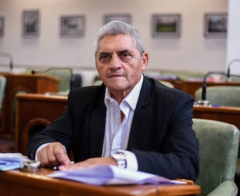 Retrato de Alberto Montes, un hombre de mediana edad con cabello gris, traje oscuro y camisa blanca, sentado en un escritorio de madera en una sala de reuniones