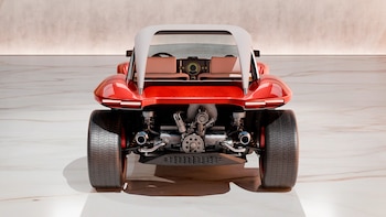 Vista trasera de un Buggy rojo brillante con techo blanco, motor expuesto y asientos beige, estacionado en una superficie clara y reflectante