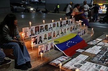 Vigilia nocturna: Una mujer sentada frente a retratos de hombres, rodeados de velas encendidas y una bandera venezolana plegada en escalones de concreto