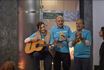 María Abadi toca la guitarra acústica, mientras Gabriel Goity y Guillermo Francella, ambos con camisetas azules "AyuDando", aplauden a su lado
