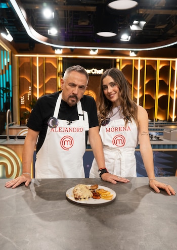 Alejandro Lerner y Morena Beltrán usan delantales blancos con sus nombres frente a un plato de comida en una cocina de televisión