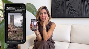 Una mujer sentada en un sofá sostiene un teléfono móvil que muestra la fotografía de un edificio parcialmente derrumbado entre escombros y vegetación.