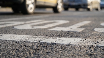 Plano a ras de suelo del asfalto rugoso con líneas blancas de señalización vial pintadas y automóviles desenfocados en el fondo.