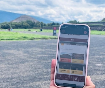 Mano sostiene un smartphone rosado con una aplicación de mapa en primer plano; al fondo, la Pirámide del Sol de Teotihuacán bajo un cielo nublado