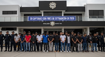 Grupo de 15 hombres esposados y policías de la Policía Nacional Civil de Guatemala frente a un edificio con cartel de 30 capturas.