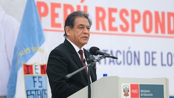 Un hombre trajeado habla frente a un micrófono en un podio con el logotipo del Ministerio de Educación de Perú