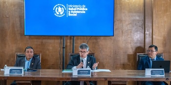 Tres hombres sentados en una mesa, un panel de madera detrás, una pantalla azul con el logo del Ministerio de Salud Pública de Guatemala