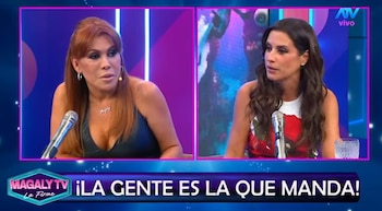 Dos mujeres sentadas en un estudio de televisión, cada una con un micrófono. Una pantalla dividida al fondo. Un zócalo azul con texto blanco