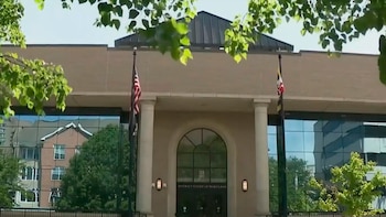 Exterior del Tribunal de Distrito de Maryland: fachada de ladrillo, columnas, entrada arqueada, ventanas de cristal. Banderas de EE. UU. y Maryland. Follaje verde